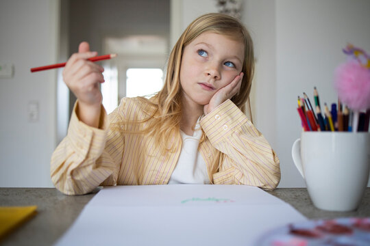 Pensive Young Girl Looking Up While Holding a Pencil and Drawing