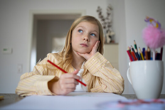 Pensive Young Girl Looking Up While Holding a Pencil and Drawing