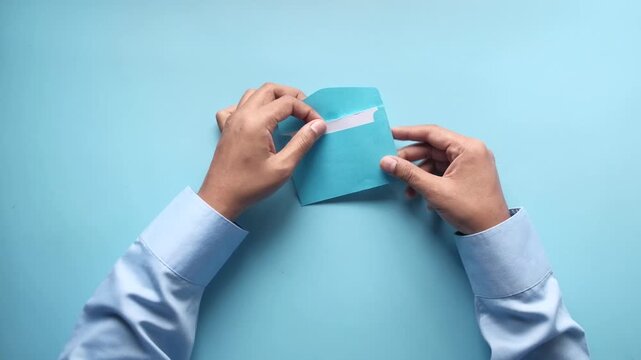 Hands opening blue envelope to reveal thank you card on light blue background top view footage