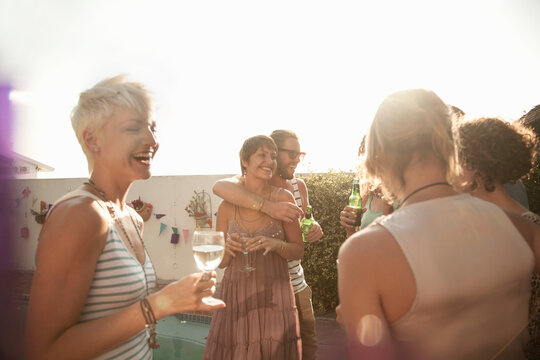 Female and male friends enjoying summer while drinking alcohol against sky