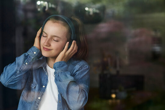 Pre-adolescent girl with eyes closed enjoying music listening through headphones at home