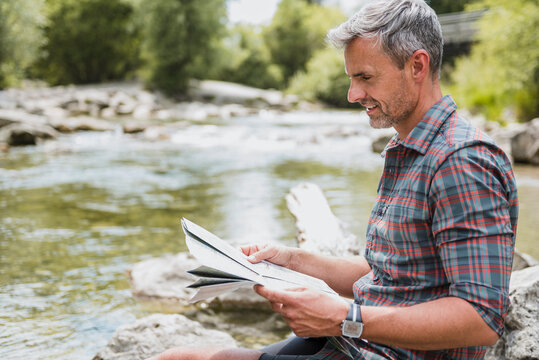 Hiker sitting at riverbank reading map