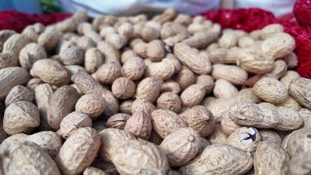Pile of unshelled peanuts in a red net bag, close-up view, dynamic camera movement