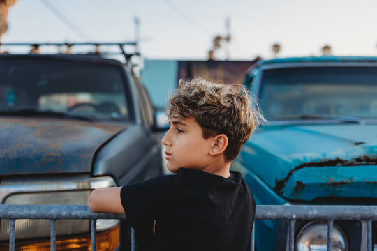 Boy on a fence with old cars on the other side.