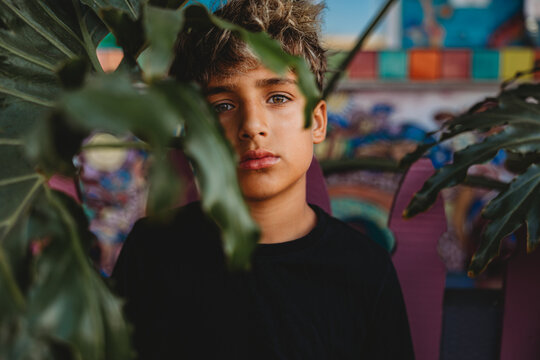Serious boy standing behind a large green leaf.