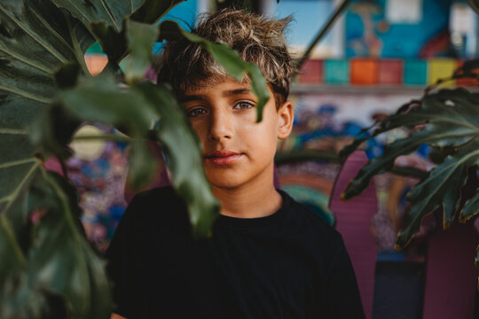 Serious boy standing behind a large green leaf.