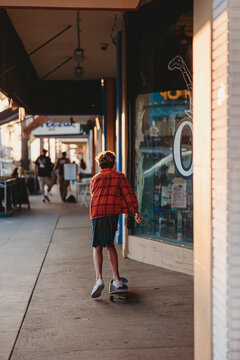 Back of a boy riding his skate board on a busy street.