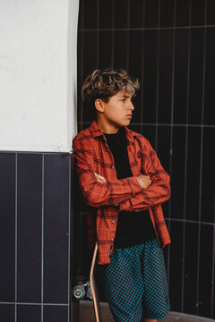 Boy with arms crossed leaning against a black tiled wall.