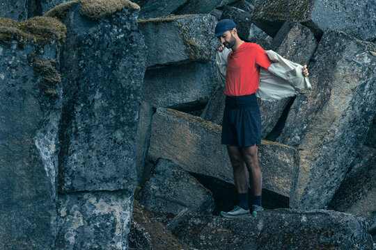 Trail runner on rocky landscape puts on technical windbreaker