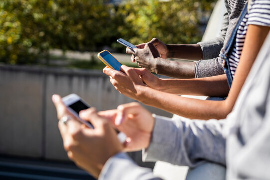 Friends standing side by side, using smartphones