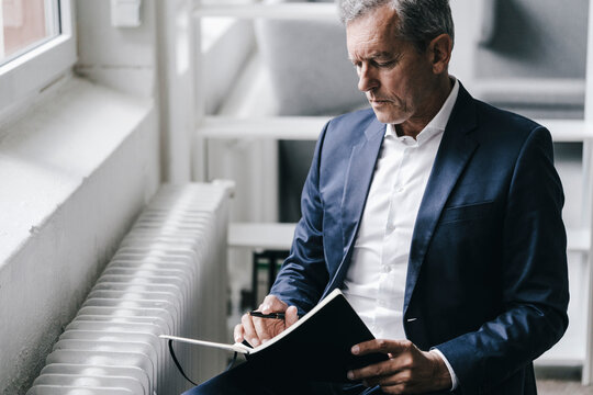 Pensive businessman with notebook sitting beside window