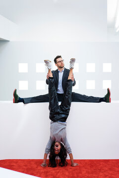 Businessman in office holding woman's legs doing a handstand