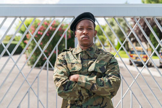 Confident army soldier standing with arms crossed against gate