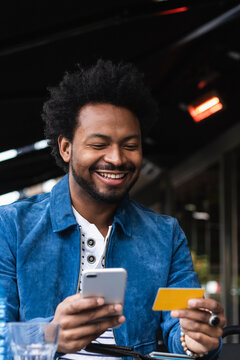 Smiling man using credit card and smart phone for paying at sidewalk cafe