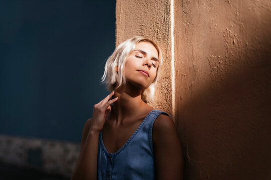 Portrait of young blond woman leaning against wall enjoying sunlight
