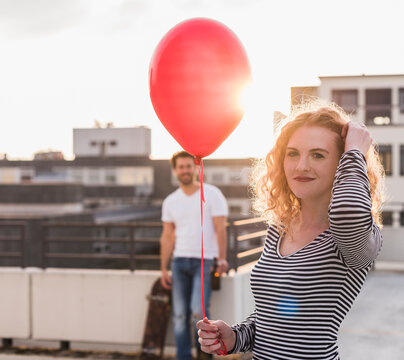 Portrait of smiling young wo man with red balloon on roof terrace at sunset