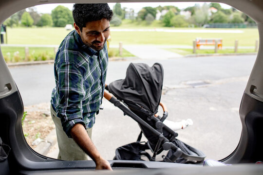 Indian man unloading pram from car boot