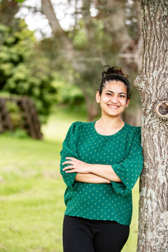 Happy Indian woman leaning against the tree with arms crossed in the park