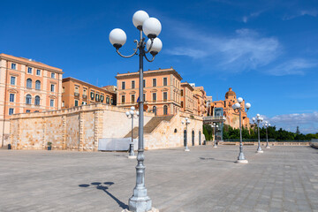 Bastione San Remy square in Cagliari, featuring a spacious paved plaza with elegant street lamps. In background, historic buildings with prominent staircase lead up to a structure with a dome