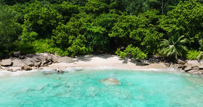 A small sandy beach with clear turquoise water surrounded by dense green vegetation and rocks. Seychelles, Mahe. Anse Major.
