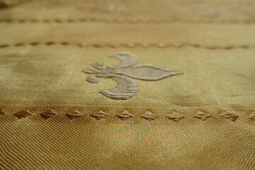 Close up of beige fabric with embroidered fleur de lis symbol © Anna