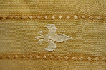 Texture of beige fabric with embroidered fleur de lis symbol © Anna