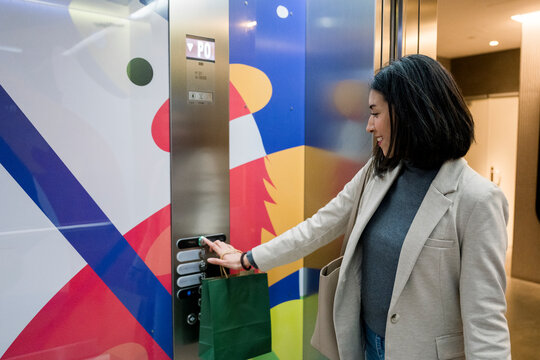 Woman using elevator with shopping bag in modern indoor setting
