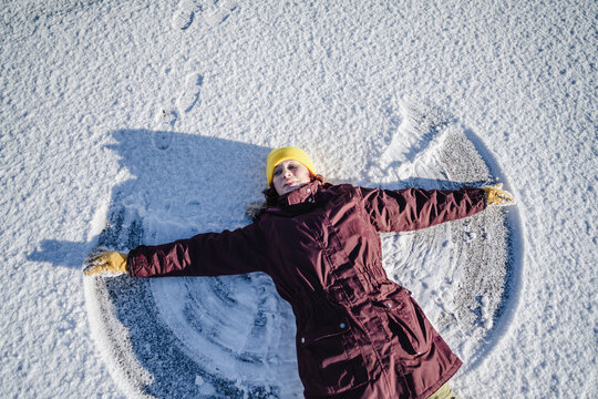 Teenager making a snow angel outdoors smiling happily in winter