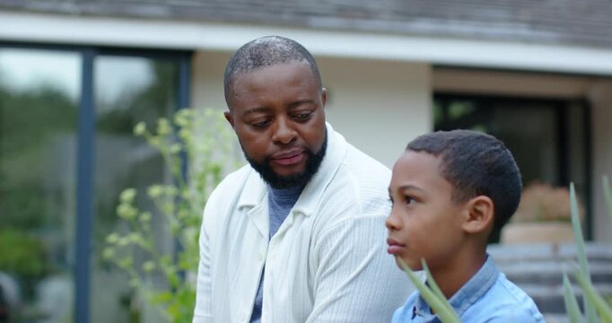 African American dad and son on patio with plants, dad leaning after pause, comforting, son smiling
