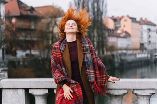 Red-haired woman tossing hair joyfully outdoors in urban city life