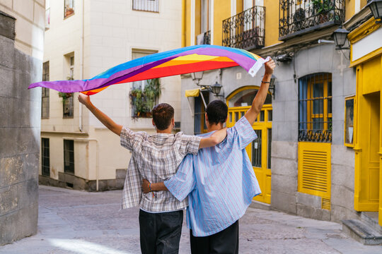 Two young men walking together, holding a rainbow flag overhead, celebrating lgbtq plus pride, inclusion, and freedom