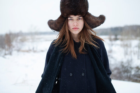 Woman in fur ushanka hat standing outdoors in snowy winter landscape