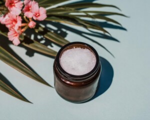 Beauty product scrub in amber glass jar resting on mint green background with floral shadows and palm leaves for natural organic skincare cosmetics branding mockup