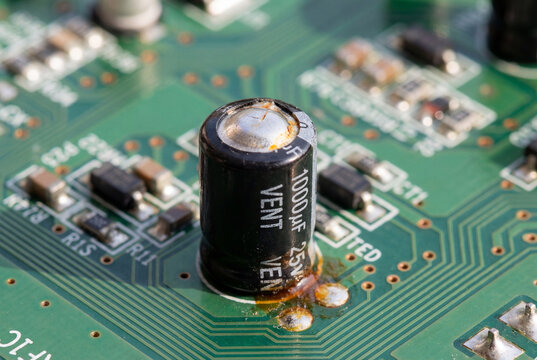 Blown electrolytic capacitor with leaked brown fluid on green computer printed circuit board
