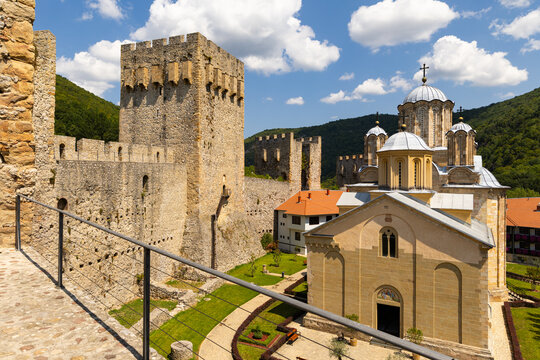 Built in elegant Morava architectural style, Church of Holy Trinity in courtyard of Manasija Monastery enclosed by manicured summer gardens, ancient stone walls with Despots Tower and forested hills