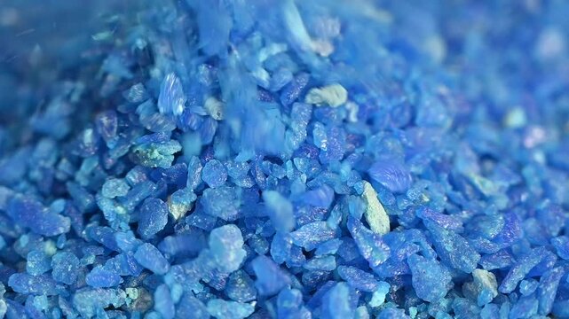  vibrant blue crystals pouring down in a continuous stream and forming a shimmering heap. The sparkling texture and rich color create a mesmerizing abstract scene, ideal for themes related to luxury