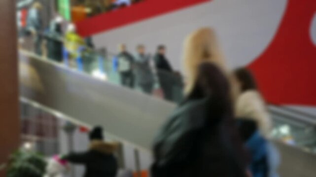 A crowd of people on fast-moving escalators in a modern shopping mall. Blurred background and unrecognizable shoppers.