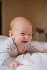 Joyful red-haired baby laughing and smiling on a soft white bed in star-print pajamas, cuddly and carefree during tummy time, capturing pure innocent childhood delight