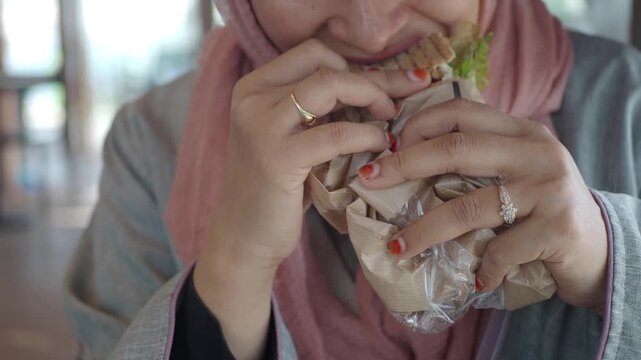 Muslim woman in hijab eating grilled sandwich held in hands with henna nails