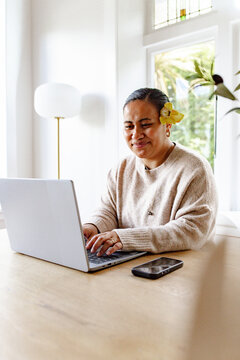 woman with flower on her ear working on her laptop on the table