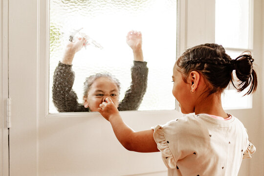 Playful Samoan boy pressing his face against the textured glass door with sister pointing his nose