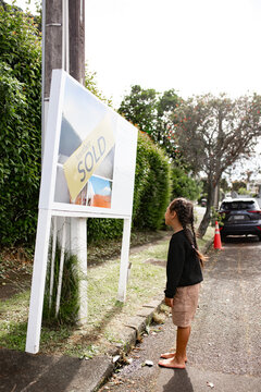 Samoan boy standing barefoot in front of real estate sign marked "SOLD"