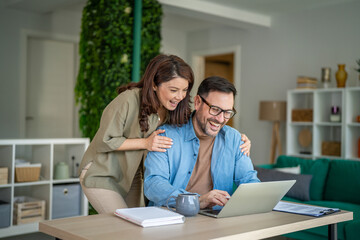 Obraz premium Happy couple working together in home office using laptop