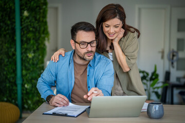 Couple planning finances and reviewing documents on laptop at home © Miljan Živković