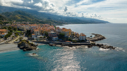 Fototapeta premium Aerial view of a historic coastal village in Italy, with traditional multi-story buildings and terracotta roofs clustered on a rocky cliff overlooking the blue sea. It is Diamante, in Calabria.
