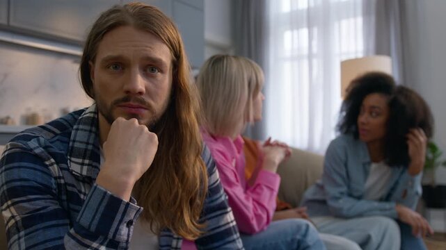 Depressed Caucasian man think at home solving problem anxious male feeling isolated antisocial avoiding friends introvert suffering ignoring social life while multiethnic women men having fun together
