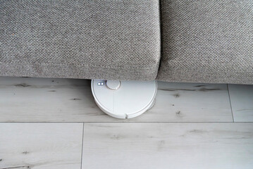 White robot vacuum cleaner cleaning under sofa