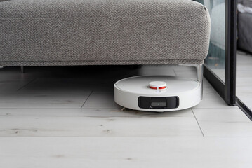 Robot vacuum cleaner under sofa in modern living room