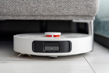 White robot vacuum cleaner cleaning under sofa