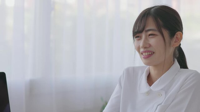 Smiling Young Woman in White Uniform Talking with Patient